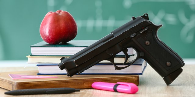 Pistol, apple and stationery on table in classroom. Concept of s