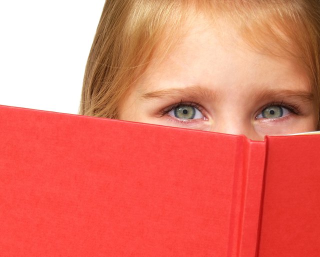 child hiding behind book